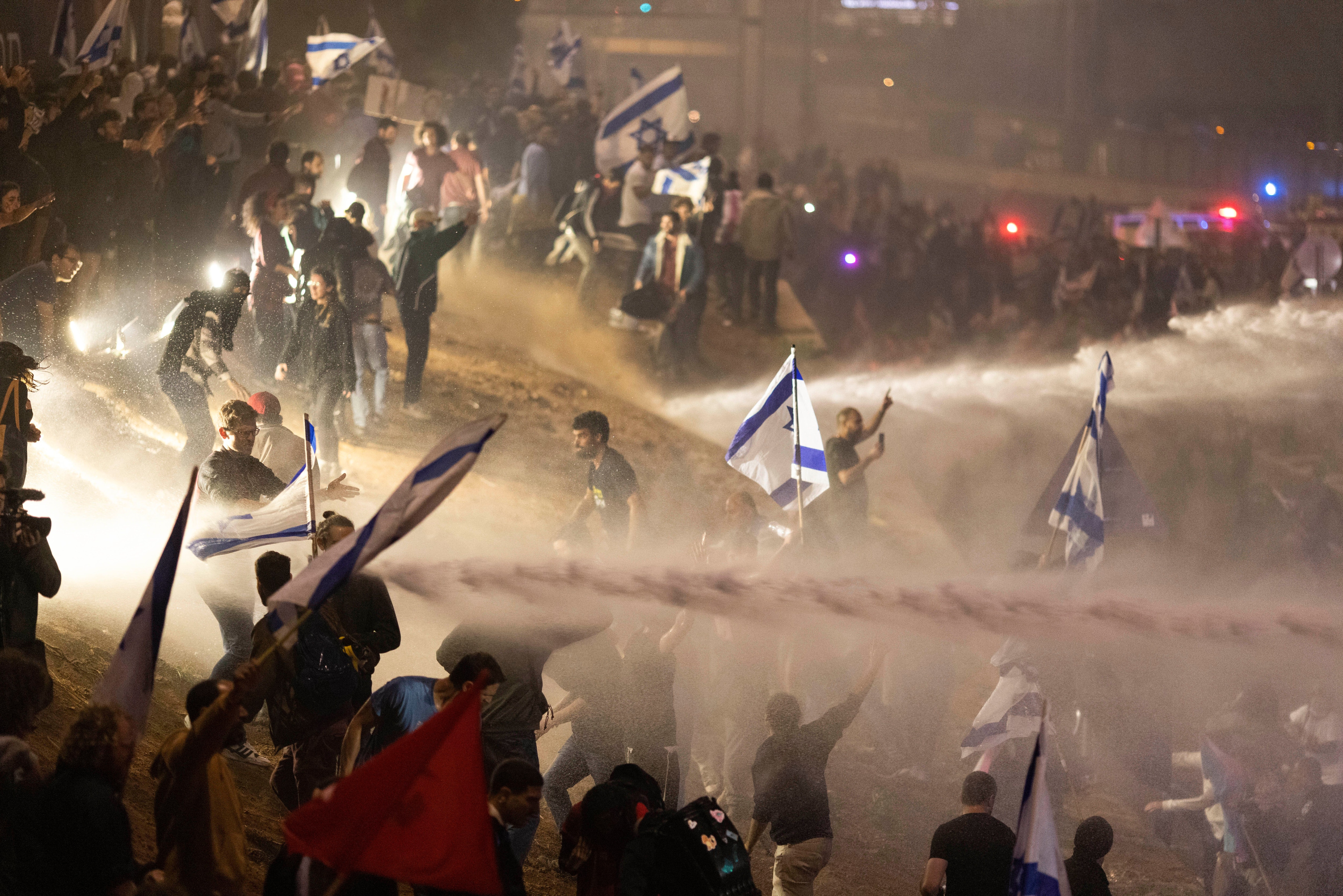 Policías israelíes emplean un cañón de agua para dispersar a los manifestantes que cortan una autopista durante una protesta contra los planes del primer ministro, Benjamin Netanyahu, de reformar el sistema judicial del país, en Tel Aviv, Israel, el lunes 27 de marzo de 2023. (AP Foto/Oren Ziv)