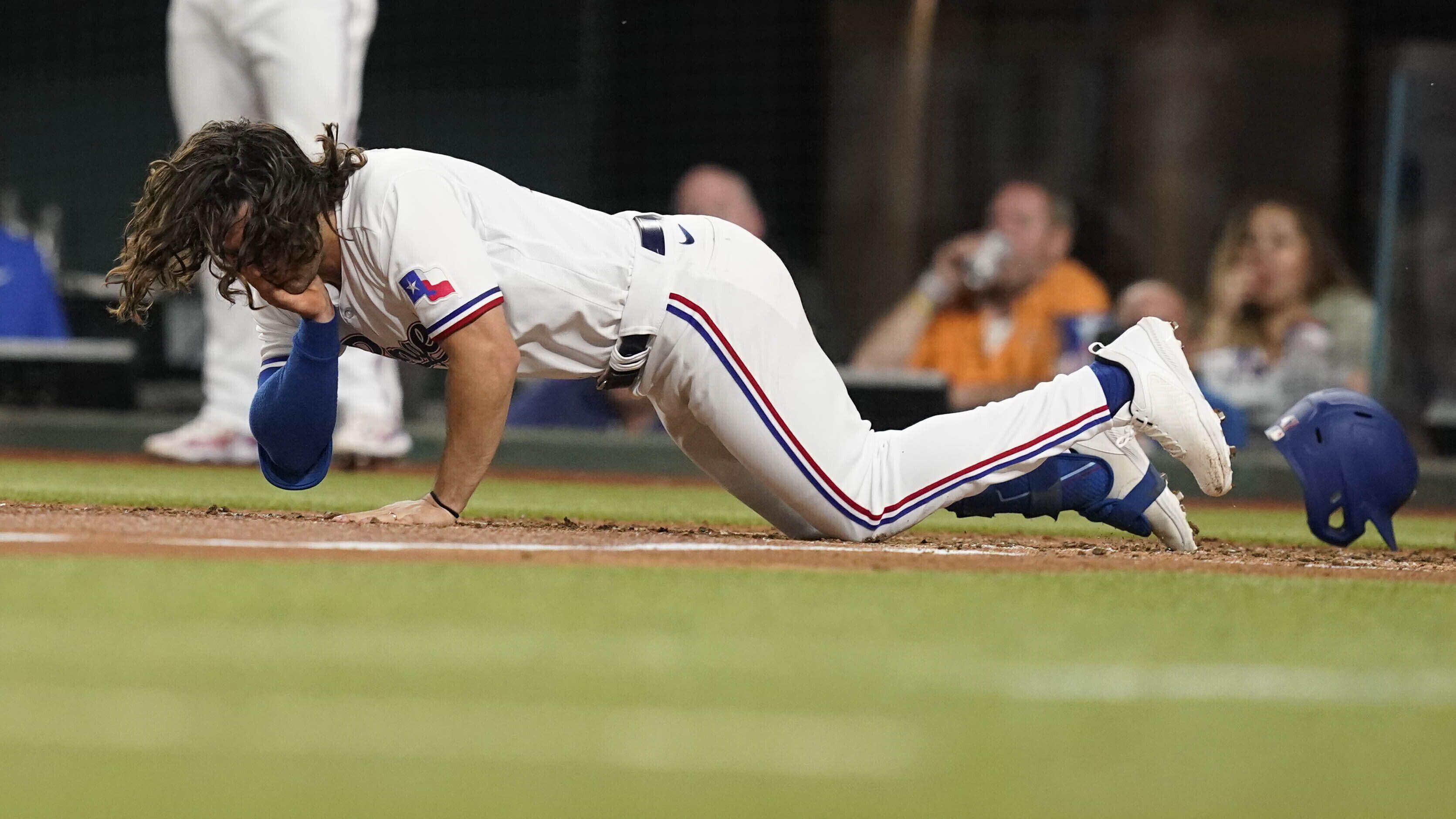 Josh Smith, de los Rangers de Texas, cae después de haber sido golpeado en la cara por un lanzamiento durante la tercera entrada del juego de béisbol en contra de los Orioles de Baltimore, en Arlington, Texas, el lunes 3 de abril de 2023. (AP Foto/LM Otero)